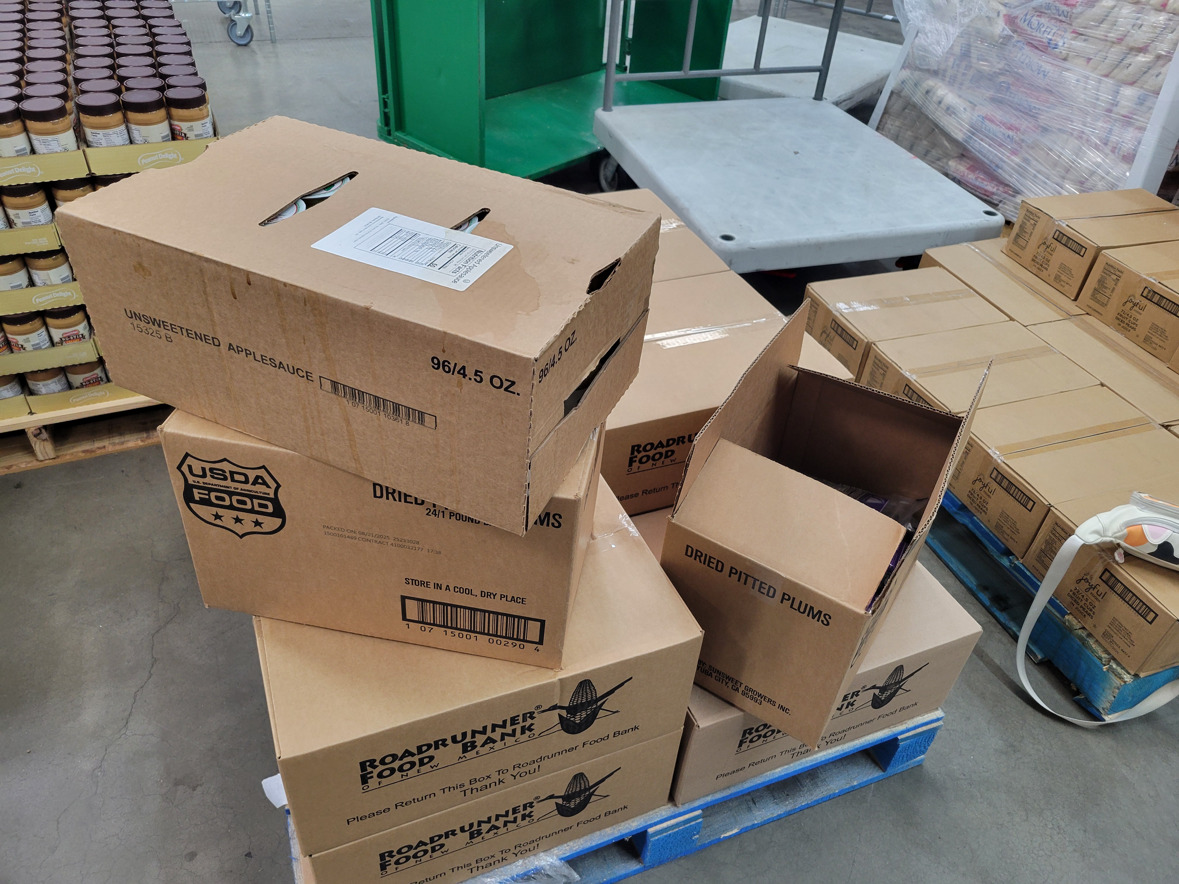 Cardboard boxes of sweetened applesauce and dried pitted plums on top of dry goods boxes.
